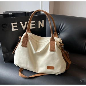 Detail of canvas tote bag showing brown logo patch and durable zipper on black sofa