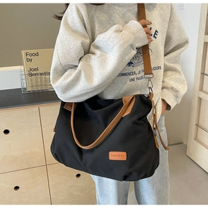 Detail of black canvas tote bag showing contrast brown straps and leather logo tag