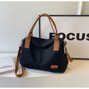 Detail of black canvas tote bag showing brown handles, adjustable strap and logo patch