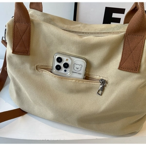 Detail of canvas tote bag showing the front zipper pocket holding a smartphone