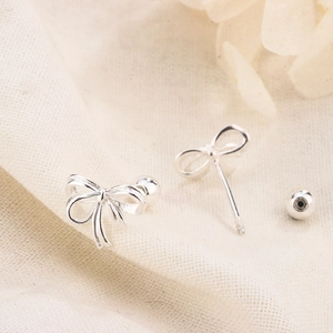 Elegant silver ribbon bow stud earrings with screw ball backs on textured fabric