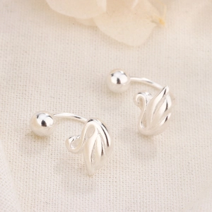 Close-up of silver swan hook earrings on linen fabric with decorative petals