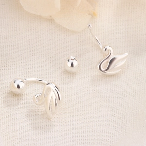 Close-up of silver swan stud earrings with screw back on textured fabric background