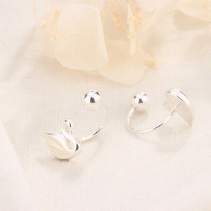 Macro view of silver swan and heart earrings with round ball backings on linen