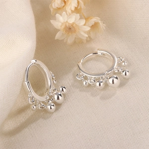 Detail view of silver geometric hoop earrings with dangling metal beads on soft fabric