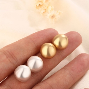 Close-up of matte gold and silver dome stud earrings held in hand for size display