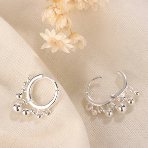 Silver geometric hoop earrings with polished bead tassels on textured fabric background