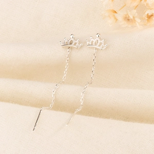 Detailed close-up of silver crown tassel earrings on soft textured linen background