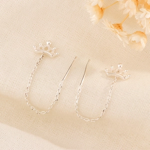 Detail of silver crown drop threader earrings on textured fabric with dried flowers