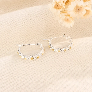 Détail des boucles d'oreilles créoles marguerites argentées avec cœur doré sur lin