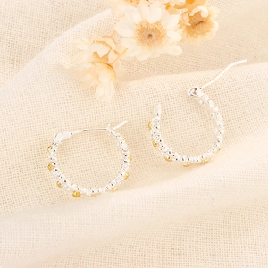 Vue macro de boucles d'oreilles créoles argentées avec détails de perles dorées