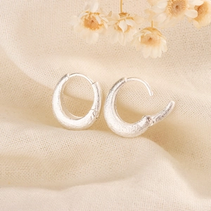 Macro detail of silver oval hoop earrings with brushed matte finish on linen background