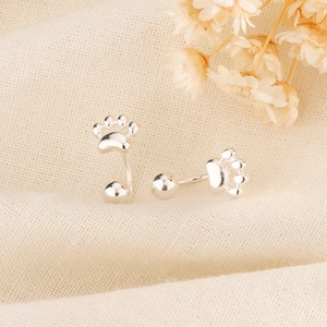 Detailed view of silver cat paw stud earrings on beige canvas with dried flowers