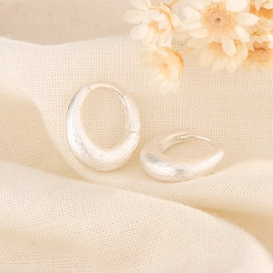 Detail of silver matte textured hoop earrings on warm knit fabric with dried flowers