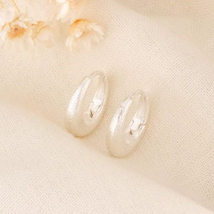 Macro shot of matte brushed texture on silver hoop earrings over beige linen fabric