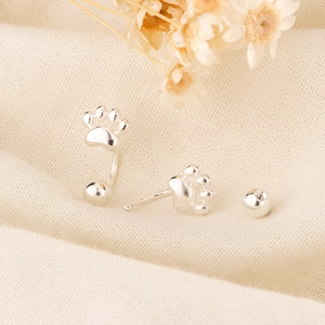 Macro shot of cute cat paw screw back earrings on a textured fabric background
