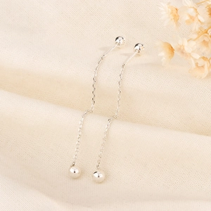 Close-up of minimalist silver ball tassel earrings on a soft textured fabric background