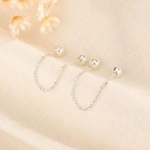 Detail view of silver bead chain earrings with screw backs on textured fabric surface