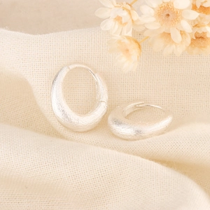 Minimalist matte silver oval earrings with brushed texture on cream linen fabric