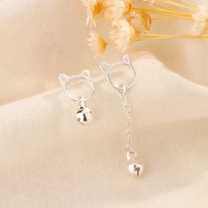 Detailed view of asymmetric silver cat bell earrings with long tassel chain on linen