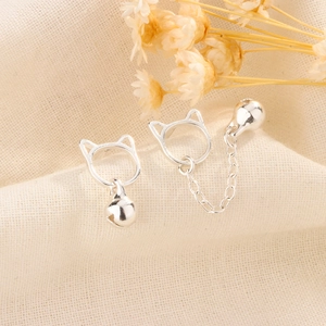 Macro shot of silver cat earrings with bells and tassels on a natural linen background