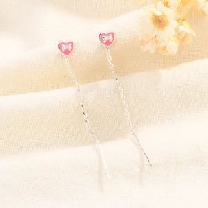 Detail of pink heart stud earrings with white bow and long silver tassel chain