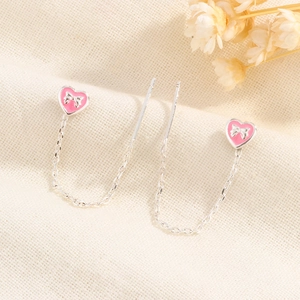 Detailed close-up of long tassel heart earrings with pink enamel and silver bow accents