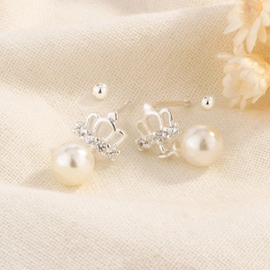 Gros plan sur d'élégantes boucles d'oreilles couronne avec diamants et perles rondes