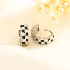 Macro detail of black and white checkerboard enamel hoop earrings on beige linen