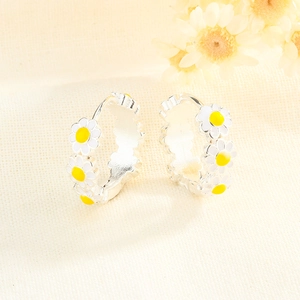 Détail des boucles d'oreilles marguerites avec pétales en émail blanc sur tissu texturé