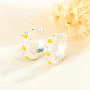 Gros plan de boucles d'oreilles créoles marguerites en argent sur un tissu en lin doux