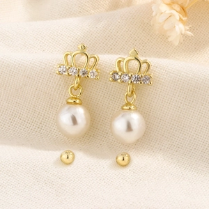 Boucles d'oreilles couronne dorées avec perles blanches et strass sur lin beige
