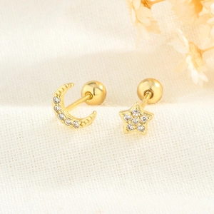 Close-up of gold moon and star stud earrings with white zircon on white textured fabric