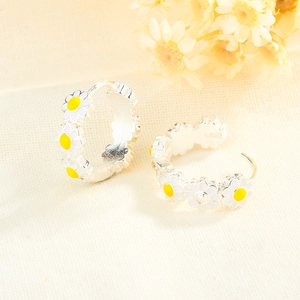 Boucles d'oreilles créoles marguerites en émail blanc et jaune sur fond de tissu beige