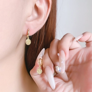 Detailed close-up of golden Fu character pendant hoop earrings on model ear