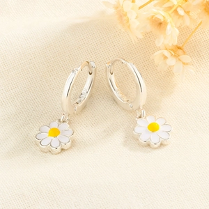 Silver daisy flower drop earrings with white enamel petals on a textured fabric background