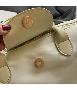 Close-up of golden magnetic snap closure on a beige nylon handbag with leather flap