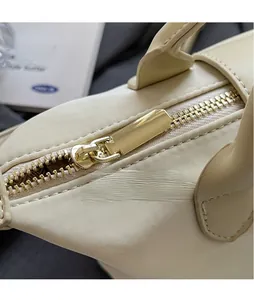 Detail of smooth gold hardware zipper head on beige Oxford fabric handbag closure