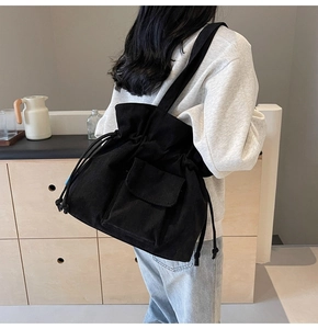 Detail of black corduroy tote bag featuring drawstring closure and front flap pocket
