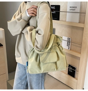 Detail of light green corduroy shoulder bag featuring a drawstring closure and front pocket