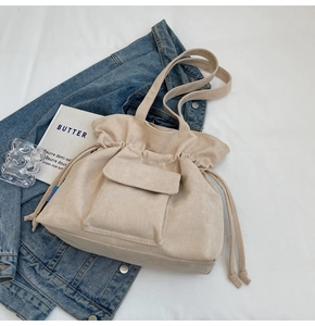 Detail of beige corduroy tote bag with drawstring closure and front pocket on white fabric