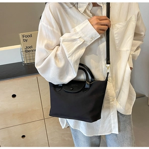 Detail of black waterproof nylon tote bag with leather handles and gold-tone hardware