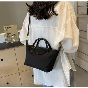 Detail of black nylon tote bag with leather handles and gold hardware shown on a model