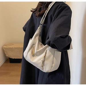 Detail view of cream canvas hobo bag with front zip pockets on model in black coat