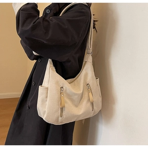 Detail view of the cream canvas dumpling bag showing its functional side pockets and zippers