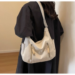 Detail of off-white canvas tote bag with side pockets worn over a black trench coat