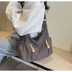 Detail of dark brown canvas shoulder bag with multiple functional zippers worn by a model