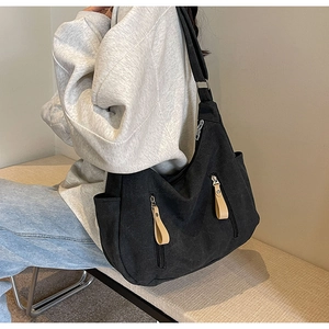 Side view of large black canvas crossbody bag with multiple zippers worn by model