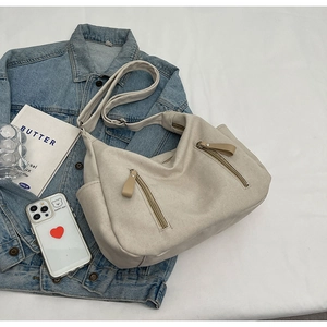 Detail of a beige canvas crossbody bag with twin zip pockets on a blue denim jacket