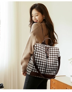 Detailed view of houndstooth backpack showing brown leather trim and rear zipper pocket
